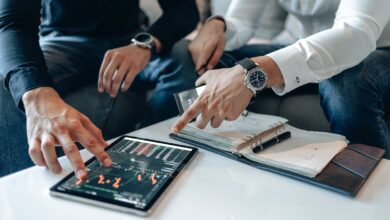 Men in business attire discussing financial data on a tablet indoors.