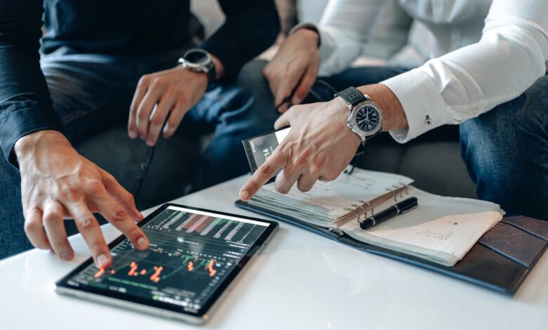 Men in business attire discussing financial data on a tablet indoors.