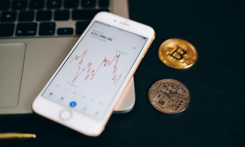 Close-up view of cryptocurrency coins and stock market graph on a smartphone screen.