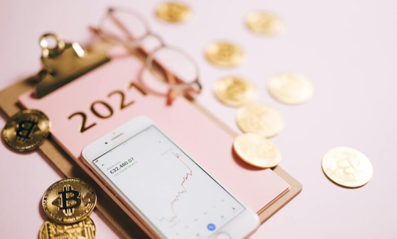 Close-up of a smartphone with crypto chart, bitcoin coins, and 2021 notepad.