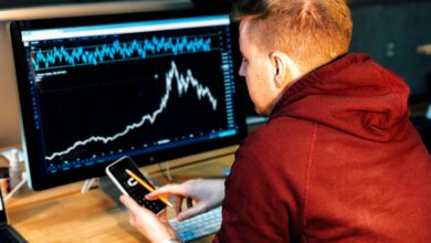 man holding black smartphone with flat screen monitor in front